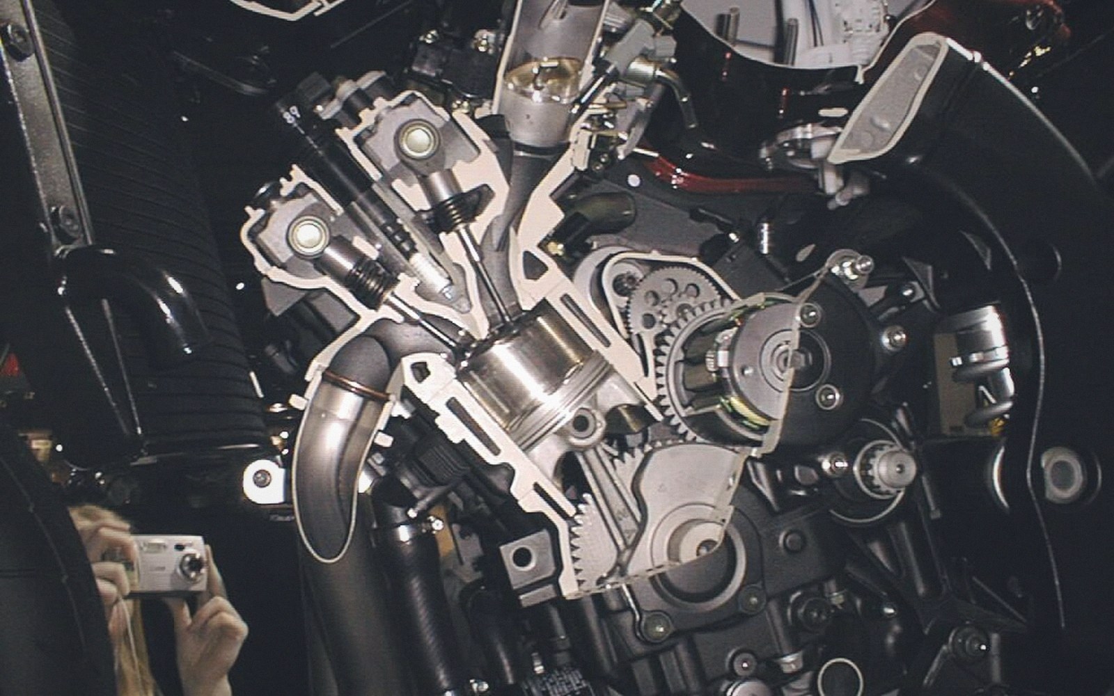 Cutaway motorcycle engine display showing piston, cylinder, valves and timing gears